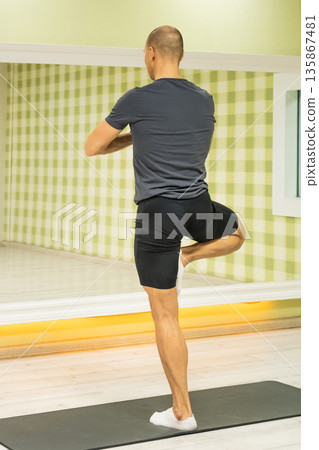 Back view of man performing yoga balance pose indoors Back view of man performing yoga balance pose indoors 135867481