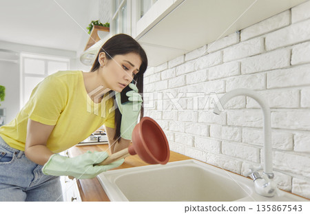 Young girl talking by the phone advising how to unclog a sink drain in the kitchen at home. Young girl talking by the phone advising how to unclog a sink drain in the kitchen at home. 135867543