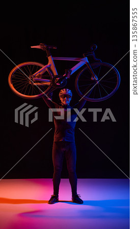 Athlete holding road bicycle overhead in studio with dramatic lighting 135867555
