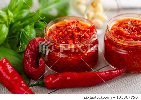 Bright red pepper condiment in jars with fresh ingredients Bright red pepper condiment in jars with fresh ingredients 135867750