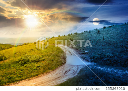 country dirt road through mountains. day and night time change concept. scenic view of green rolling hills under sky with clouds with sun and moon at twilight. duality and transition template 135868010