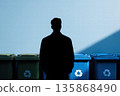 Silhouette Of Man Standing By Recycling Bins In Front Of Blue Wall 135868490