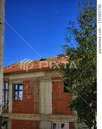 A rural house under a blue sky. An unfinished brick building. A house under construction. A house renovation. A rural house under a blue sky. An unfinished brick building. A house under construction. A house renovation. 135868796