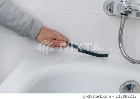 a man cleans the bathtub tile grout 135869212