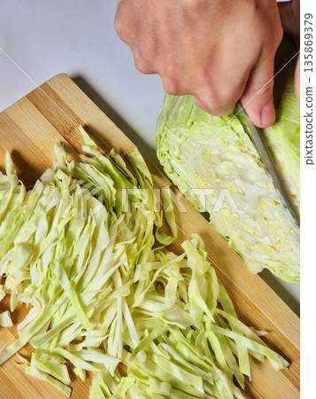 Hands Chopping Cabbage on a Wooden Board. Slicing Fresh Cabbage for a Salad. Food Prep: Close-up of Chopping Vegetables. Hands Chopping Cabbage on a Wooden Board. Slicing Fresh Cabbage for a Salad. Food Prep: Close-up of Chopping Vegetables. 135869379
