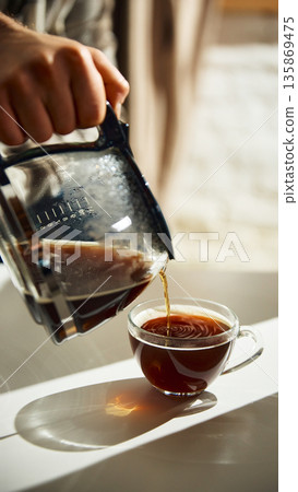 Close up of coffee pouring from pot into glass cup with steam Close up of coffee pouring from pot into glass cup with steam 135869475