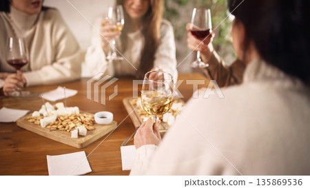 Group of friends tasting white wine at table with snacks indoors. Group of friends tasting white wine at table with snacks indoors. 135869536