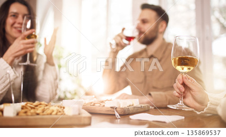 Friends enjoying white and red wine at table during casual home tasting. Friends enjoying white and red wine at table during casual home tasting. 135869537