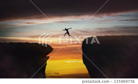 Determined man jumping over a chasm to reach the other side. Conceptual scene for overcoming obstacles and reaching new highs. Motivational and inspirational background Determined man jumping over a chasm to reach the other side. Conceptual scene for overcoming obstacles and reaching new highs. Motivational and inspirational background 135869736