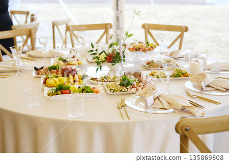 Elegant dining table set for a special event, featuring an array of gourmet dishes, fresh fruits, and decorative floral centerpiece, creating a festive atmosphere Elegant dining table set for a special event, featuring an array of gourmet dishes, fresh fruits, and decorative floral centerpiece, creating a festive atmosphere 135869808