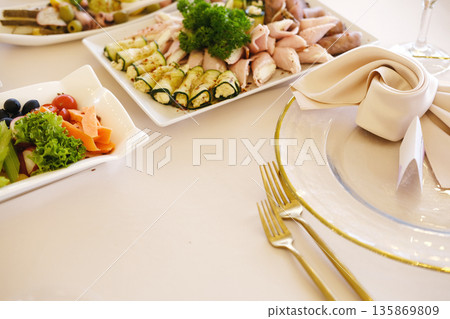 Elegant wedding table setting featuring assorted appetizers, beautifully arranged plates, fresh greens, and decorative napkins, creating a sophisticated dining experience for guests 135869809