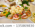 Colorful platter of assorted appetizers featuring various toppings, garnished with fresh herbs, displayed elegantly on a glass serving dish for a festive gathering or event 135869830