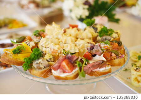Colorful platter of assorted appetizers featuring various toppings, garnished with fresh herbs, displayed elegantly on a glass serving dish for a festive gathering or event Colorful platter of assorted appetizers featuring various toppings, garnished with fresh herbs, displayed elegantly on a glass serving dish for a festive gathering or event 135869830