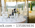 Elegant table setting with assorted wine bottles and glassware on a white tablecloth, illuminated by soft lights in a festive outdoor event atmosphere 135869836