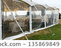 Elegant marquee tent with transparent sides, beautifully decorated for a boho outdoor wedding, showcasing tables and ambient lighting for a romantic atmosphere 135869849