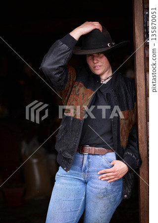 Cowgirl in black hat and denim jeans posing at a rustic ranch doorway, ready for work Cowgirl in black hat and denim jeans posing at a rustic ranch doorway, ready for work 135870051