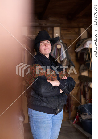 Cowgirl in a ranch setting wearing a hat and jacket with arms crossed, confident pose Cowgirl in a ranch setting wearing a hat and jacket with arms crossed, confident pose 135870079