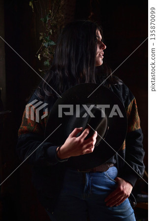 Moody portrait of a woman in a dark hat, denim jeans, and a patterned sweater Moody portrait of a woman in a dark hat, denim jeans, and a patterned sweater 135870099