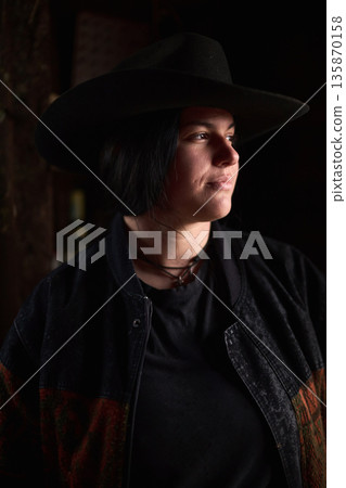 Cowgirl in a wide hat gazes into the distance at a dimly lit ranch setting Cowgirl in a wide hat gazes into the distance at a dimly lit ranch setting 135870158
