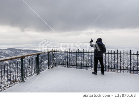 Tourist taking photo from viewpoint over snowy Brasov, Romania Tourist taking photo from viewpoint over snowy Brasov, Romania 135870168