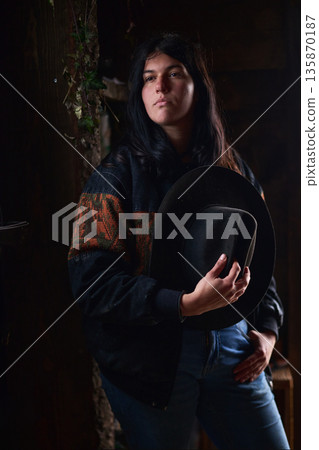 Portrait of a woman in a dark sweater holding a wide-brimmed hat in a moody setting Portrait of a woman in a dark sweater holding a wide-brimmed hat in a moody setting 135870187