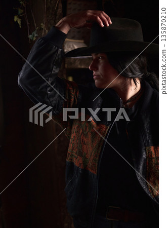 Cowgirl in Wide-Brim Hat Adjusting Her Hat in a Rustic Ranch Setting Cowgirl in Wide-Brim Hat Adjusting Her Hat in a Rustic Ranch Setting 135870210