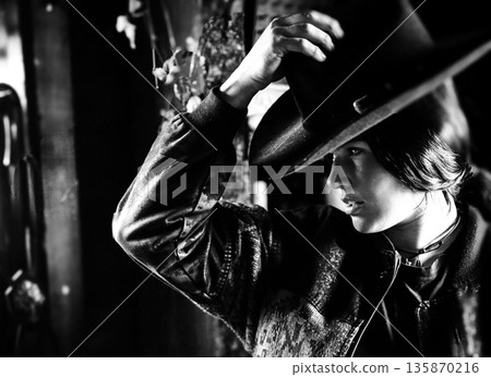 Portrait of a woman in a hat and leather jacket, captured in a dramatic black-and-white mood 135870216