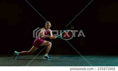 Competitive female tennis athlete lunging for shot on dark minimal background. Competitive female tennis athlete lunging for shot on dark minimal background. 135871008