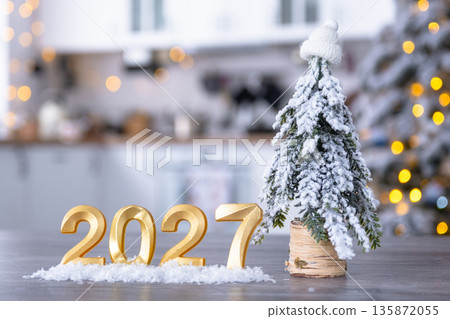 Golden number 2027 on table in background of cozy white kitchen with Christmas tree and Christmas decor with garland lights. Housing, interior, renovation, mortgage, rent in New Year Golden number 2027 on table in background of cozy white kitchen with Christmas tree and Christmas decor with garland lights. Housing, interior, renovation, mortgage, rent in New Year 135872055