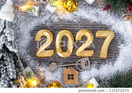 New Year 2027 golden numbers and House key with tiny form of home on festive grey wooden background flatlay, lights of garlands, greeting card. Housing, real estate, relocation, mortgage, insurance 135872073