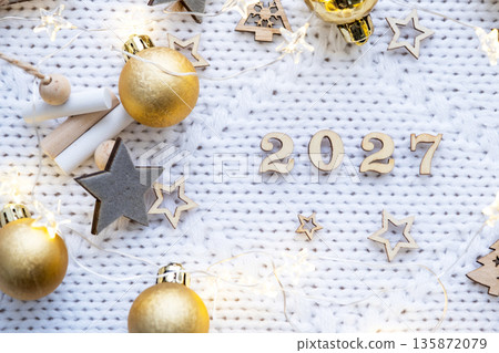 Happy New Year wooden numbers 2027 on cozy festive white knitted background with sequins, stars, lights of garlands. Greetings, postcard. Calendar, cover Happy New Year wooden numbers 2027 on cozy festive white knitted background with sequins, stars, lights of garlands. Greetings, postcard. Calendar, cover 135872079