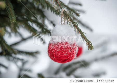 Red wool ball hanging on the green branches of a Christmas tree. 135872256