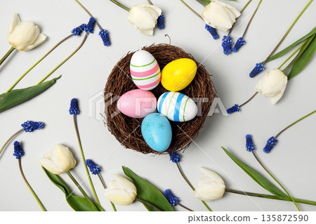 Easter colored painted eggs in bird nest with white tulips, and blue muscari on gray background. Easter and spring concept. Spring background 135872590
