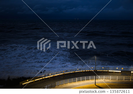 夜幕降臨，藍調時刻的波浪和燈光照耀下的蜿蜒道路 135872611
