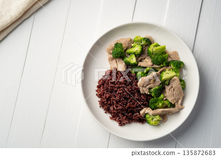 Cooked riceberry rice and Stir fried broccoli with pork tenderloin fillet in white plate.Thai Healthy food for low fat diet menu.Top view 135872683