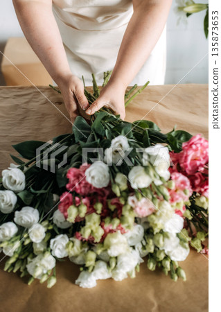 Person gathers bundles of pink and white lisianthus flowers on craft paper. Support local florists, flower farm-to-shop, urban florist. Person gathers bundles of pink and white lisianthus flowers on craft paper. Support local florists, flower farm-to-shop, urban florist. 135873653