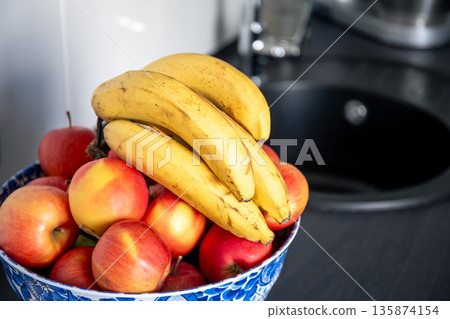 A bunch of bananas and apples in the kitchen near the sink. 135874154