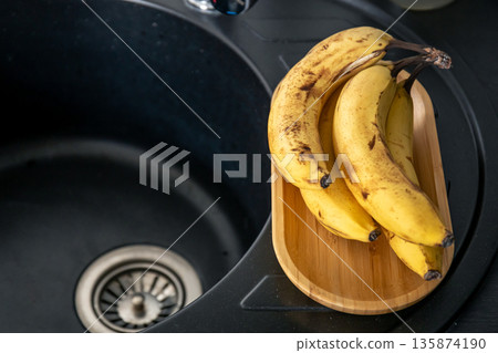 A bunch of ripe yellow bananas in the kitchen near the sink. 135874190