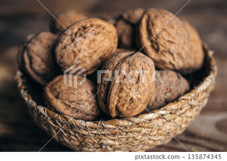 Close-up, whole walnuts in a wicker bowl on a wooden background. Close-up, whole walnuts in a wicker bowl on a wooden background. 135874345