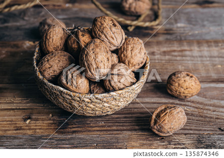 Close-up, whole walnuts in a wicker bowl on a wooden background. Close-up, whole walnuts in a wicker bowl on a wooden background. 135874346