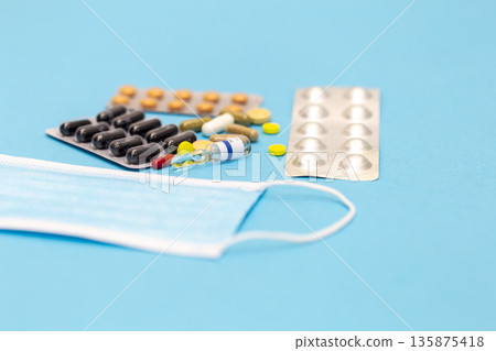 A variety of pills and a protective face mask on a blue background. A variety of pills and a protective face mask on a blue background. 135875418