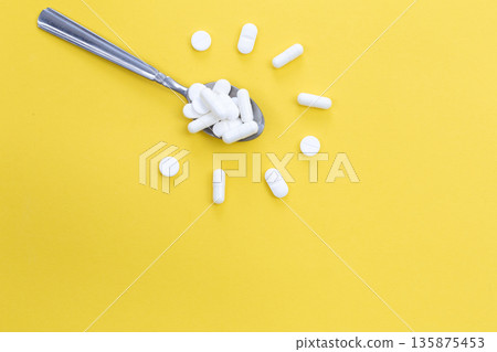 White pills in spoon in the shape of a flower on a yellow background, flat lay. White pills in spoon in the shape of a flower on a yellow background, flat lay. 135875453