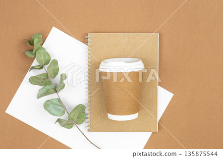 Craft paper coffee cup, notebook and eucalyptus sprig on eco background, flat lay. Craft paper coffee cup, notebook and eucalyptus sprig on eco background, flat lay. 135875544
