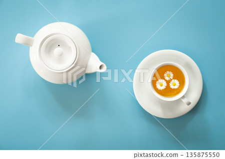 A cup of chamomile tea and a teapot on a blue background. A cup of chamomile tea and a teapot on a blue background. 135875550