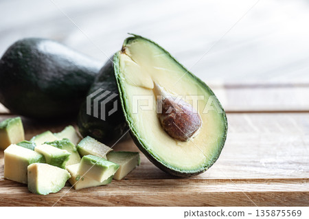 Whole ripe avocado fruit and diced close-up on a wooden surface. Whole ripe avocado fruit and diced close-up on a wooden surface. 135875569