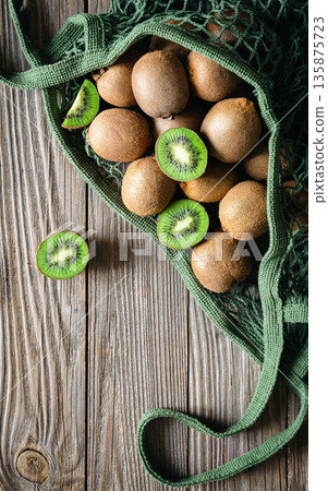 Fruits of kiwi in a mesh bag on a wooden background, top view, rustic style, Fruits of kiwi in a mesh bag on a wooden background, top view, rustic style, 135875723