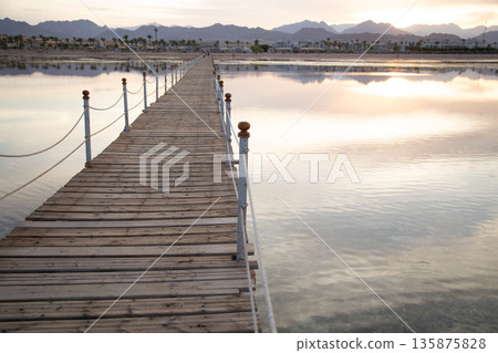 Long wooden pier among the sea at sunset. Long wooden pier among the sea at sunset. 135875828
