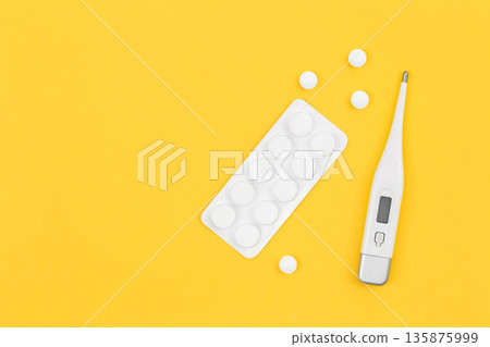 Pills and electronic thermometer on a yellow background, flat lay. Pills and electronic thermometer on a yellow background, flat lay. 135875999