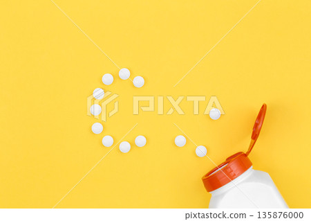 Pills laid out in C shape, on yellow background, flat lay, vitamin C concept 135876000