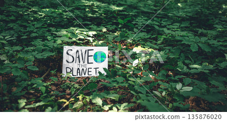 Poster with the inscription save the planet in the forest among the plants. Poster with the inscription save the planet in the forest among the plants. 135876020